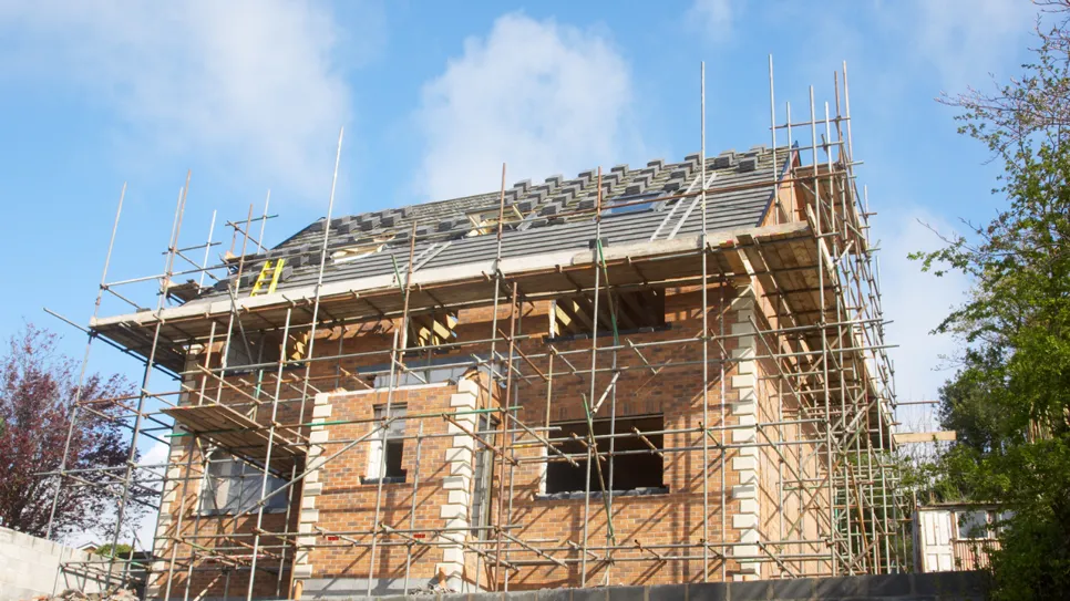Construcția unei case noi Construcție nouă din cărămidă în faza de acoperire a acoperișului, înconjurată de schele de construcție.